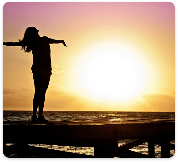 Freedom and Wellness – The Benefits of Medication Management at Regions Praxis Care Silhouette of a woman standing on a pier with arms outstretched during a vibrant sunset over the ocean.